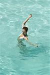 Jeune femme debout dans la piscine, qui s'étend de bras, pleine longueur, vue grand angle