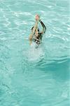 Jeune femme debout dans la piscine, éclaboussant les bras sur la tête, pleine longueur, vue grand angle