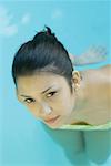 Young woman in pool wearing bikini, looking up at camera, close-up, high angle view