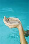 Young woman holding up cupped hands full of water, cropped view