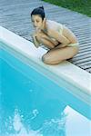Young woman in bikini crouching by edge of pool