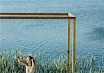 Young woman standing inside square structure, next to body of water