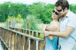 Couple standing by wooden foot bridge, man embracing woman