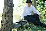 Homme assis sur un banc, sous les arbres, à l'aide de laZSop