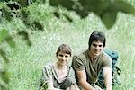 Hiking couple resting in grass, smiling at camera