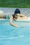 Young woman lying next to pool, touching water