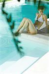 Jeune femme assise au bord de piscine, pleine longueur