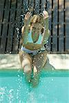 Jeune femme assise sur le bord de la piscine, projections d'eau