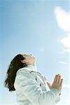 Teen girl with hands clasped, eyes closed and head back, low angle view