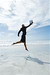 Businesswoman jumping in air on beach, holding up file