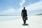 Businessman walking on beach, carrying briefcase
