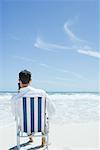 Businessman sitting in folding chair, holding up cell phone, on beach
