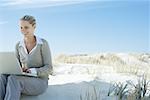 Businesswoman sitting on beach, using laZSop, looking away