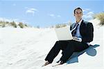 Businessman sitting on beach, using laZSop, looking away