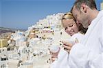 Couple in bathrobes with cups smiling with scenic village in background