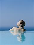 Rear view of woman in pool with eyes closed leaning