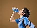 Profile of boy with backpack drinking beverage from plastic bottle