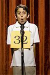 Boy standing at microphone speaking with number around neck