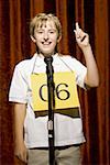 Girl contestant standing at microphone smiling and pointing up