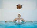 Woman sitting and leaning against wall in pool under urn
