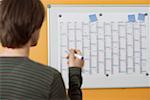 A man is standing in front of an annual calendar