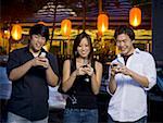 Three people with cell phones outdoors at night smiling