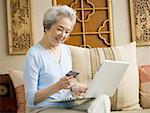 Femme assise sur le canapé avec ordinateur portable et le sourire de la carte de crédit