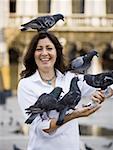 Woman in public square feeding pigeons and smiling