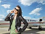 Woman standing next to private jet on phone.