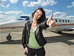 Woman giving thumbs up beside private jet.