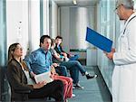 Male doctor calling for patients in hospital waiting room.