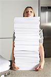 Young woman working from home with huge pile of paper.