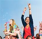 Two girls sitting on shoulders in a crowd blowing bubbles