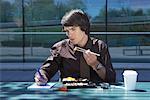 Businessman eating sushi outside while making notes.