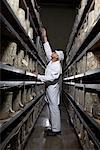 Man reaching up in between two shelves of cheeses.