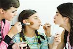 Two young female friends putting make-up on younger girl