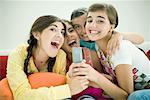 Young female friends sitting together, singing into remote control