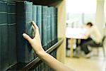 Female student taking reference book from shelf in library