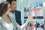 Couple standing next to window of real estate agency, looking at for rent sign