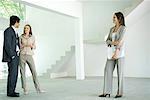 Female real estate agent standing in empty home interior with young couple, full length