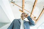 Man in suit using cell phone, bare pipes overhead, low angle view