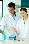 Male and female lab workers standing side by side, woman looking at camera