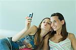 Young woman photographing self with friend, holding up cell phone