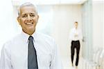 Mature businessman standing in hallway, smiling at camera, portrait