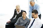 Business associates looking at laptop together, woman in center smiling at camera