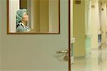 Female surgeon leaning against wall, looking up, view through window in door