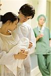 Couple standing, looking at newborn baby together, doctor in background