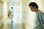 Male patient standing in hospital corridor, looking down, side view