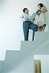 Businessman and young businesswoman standing on stairs, looking at each other, low angle view