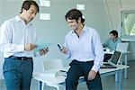 Businessmen in office, one using cell phone, smiling